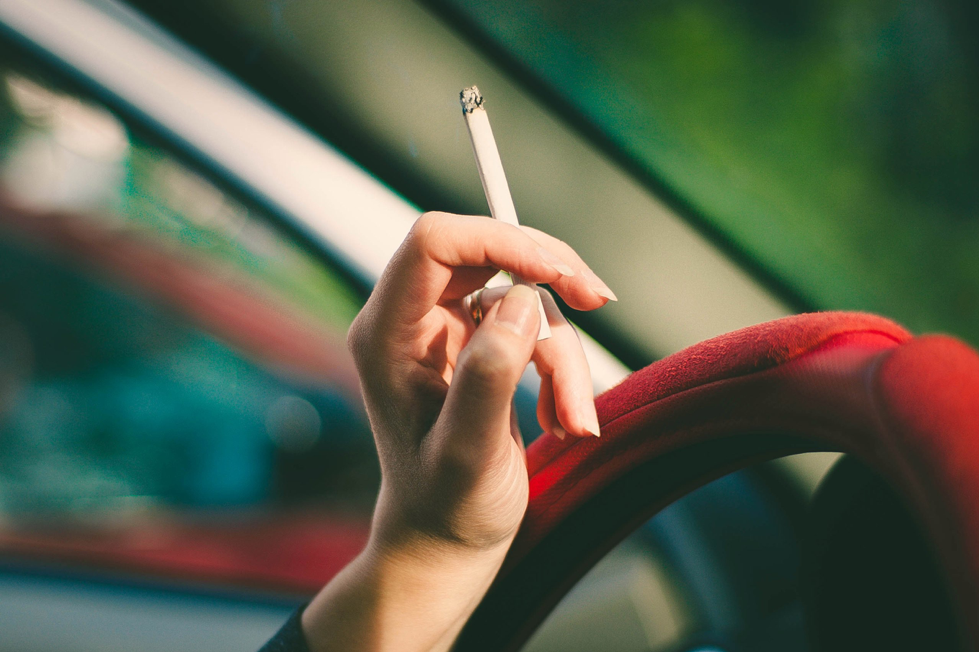 Person holding cigarette on steering wheel