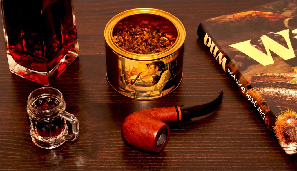 Smoking pipe on a table with tobacco, a book and two glasses of drink