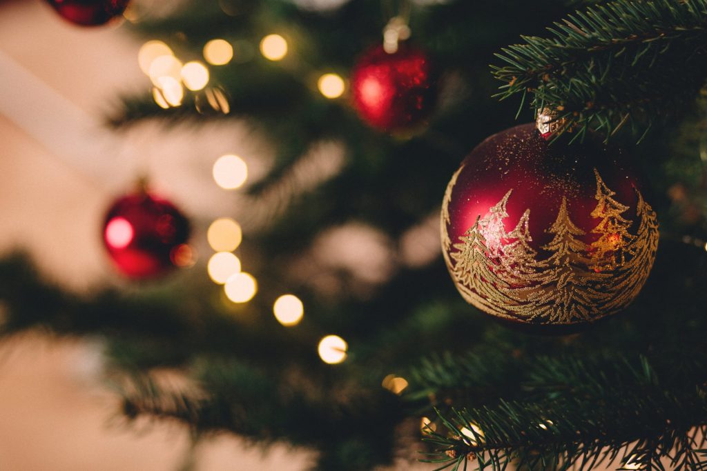 A red bauble featuring glittery golden Christmas trees hung on a larger tree